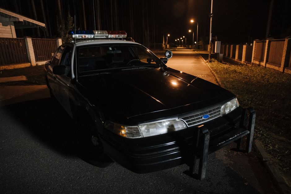 A police car parked on a quiet street at night with streetlights illuminating the road.