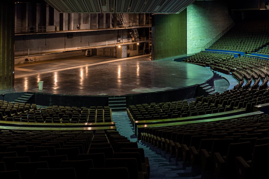 Wide-angle view of an empty theater auditorium with rows of seats facing a grand stage.