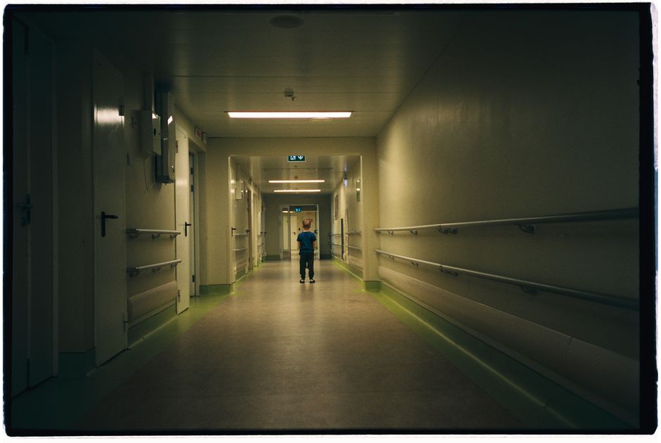 A young boy walks down an empty hospital hallway, evoking solitude and contemplation.