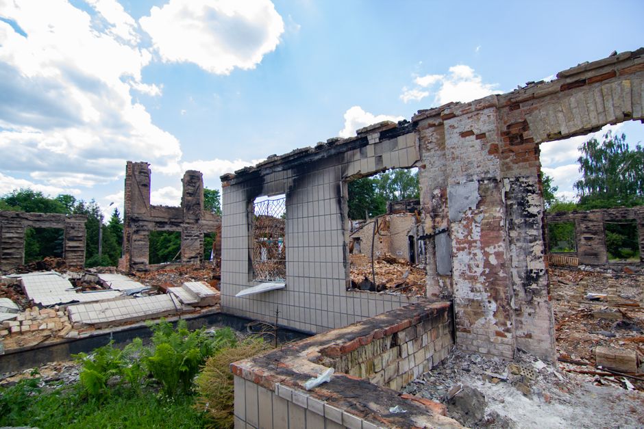 Abandoned building ruins with overgrown plants under a cloudy summer sky.