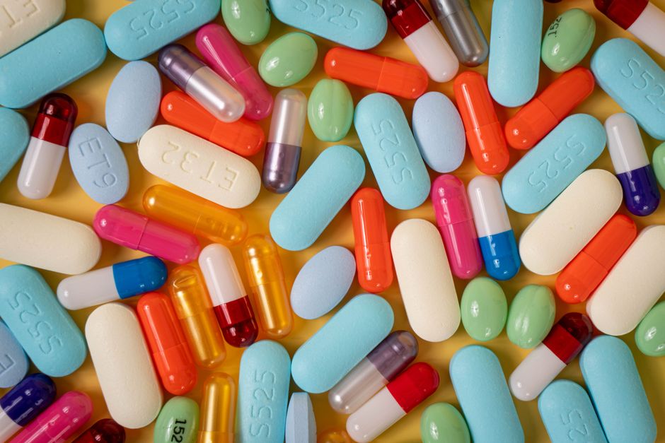 A vibrant array of various pills and capsules on a yellow background.