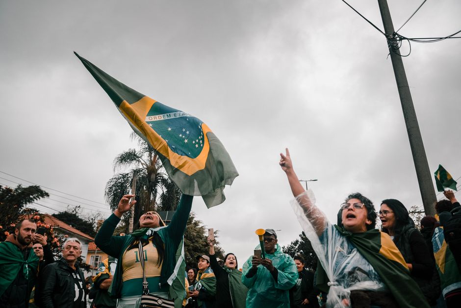 A lively demonstration with people waving Brazilian flags on a cloudy day.
