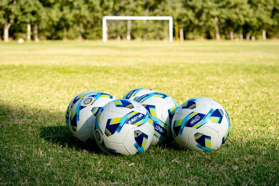 Five soccer balls rest on a green field, ready for a game in Mendoza, Argentina.