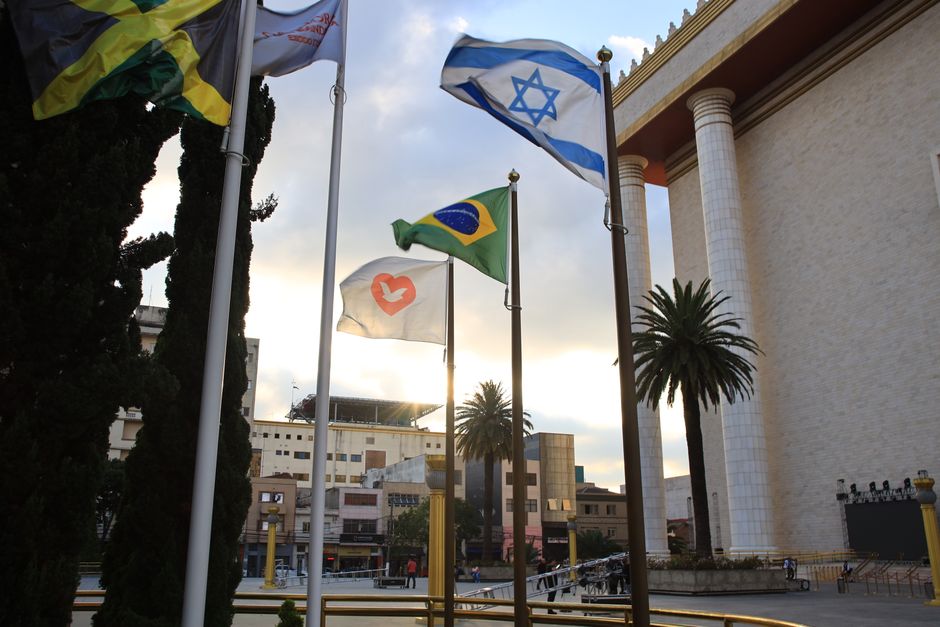 Flags waving in front of the iconic Temple of Solomon in São Paulo, Brazil, under a cloudy sky.