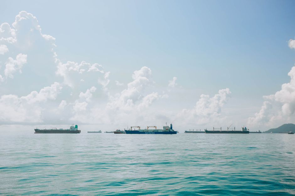 Serene view of cargo ships on the calm sea with fluffy clouds in a blue sky.