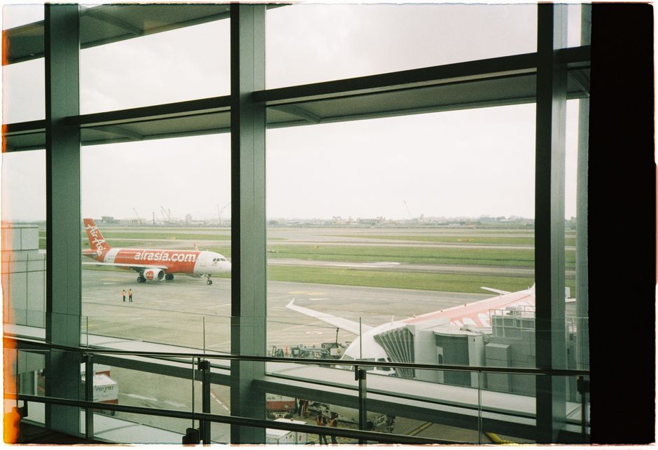 View of an AirAsia plane taxiing on the runway from inside the airport terminal.