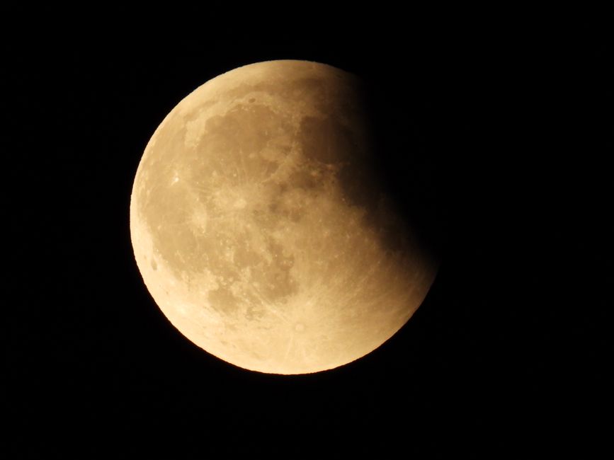 A partial lunar eclipse casting shadows on the moon's surface during a clear night in the UK.