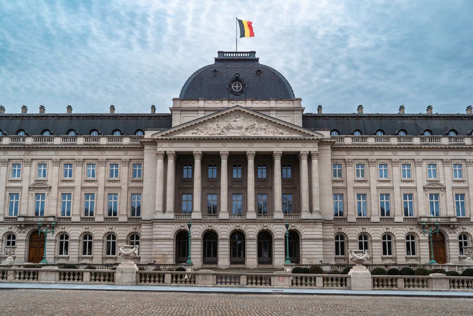 Front view of the Royal Palace of Brussels with Belgian flag under a cloudy sky.