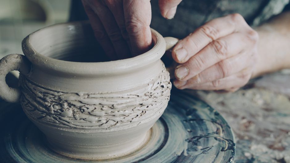 Hands of an artisan shaping a clay pot on a pottery wheel, showcasing craftsmanship.