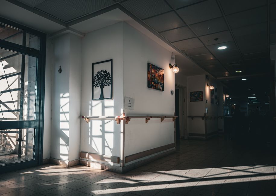 A quiet hospital corridor with sunlight streaming through, highlighting art on the walls.