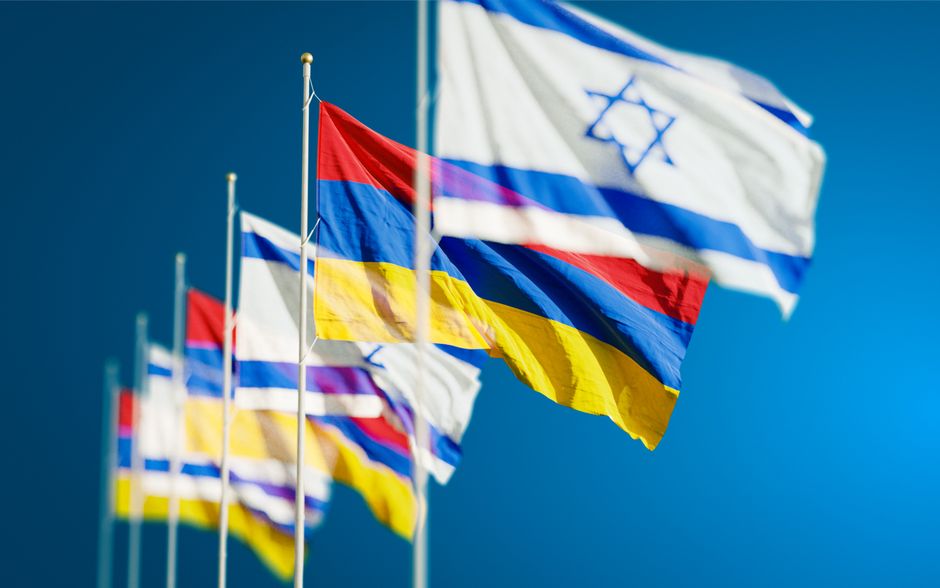 Vibrant national flags of Israel and Armenia waving against a clear blue sky.