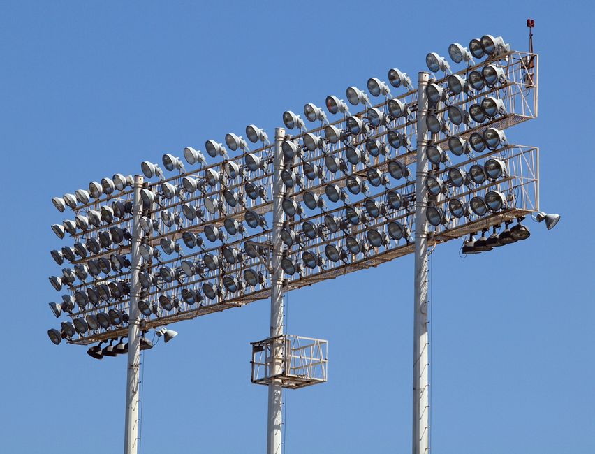 A low angle shot of towering stadium floodlights set against a clear blue sky.