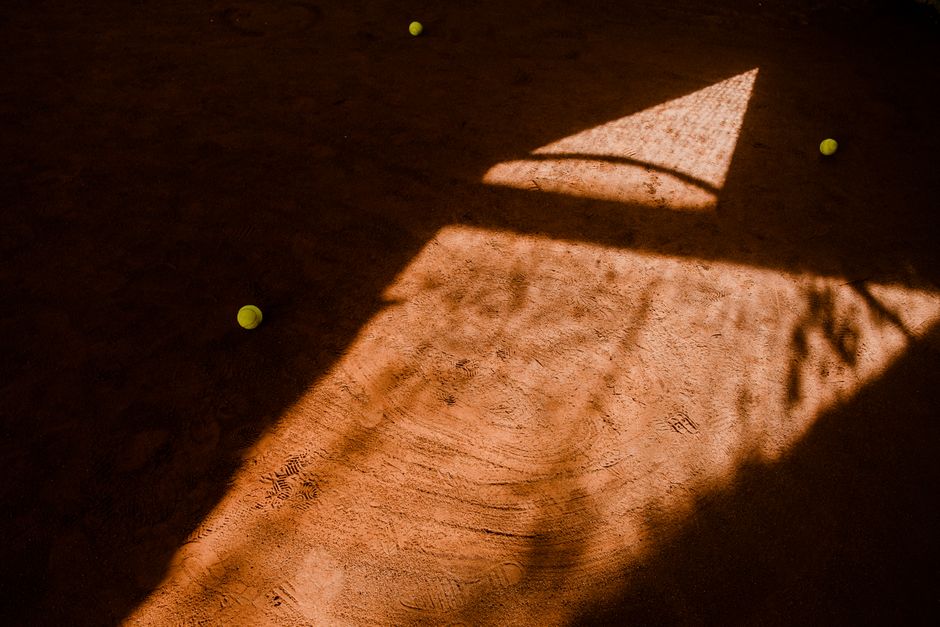 Artistic shadows cast over a tennis court with balls scattered, creating a moody sports scene.