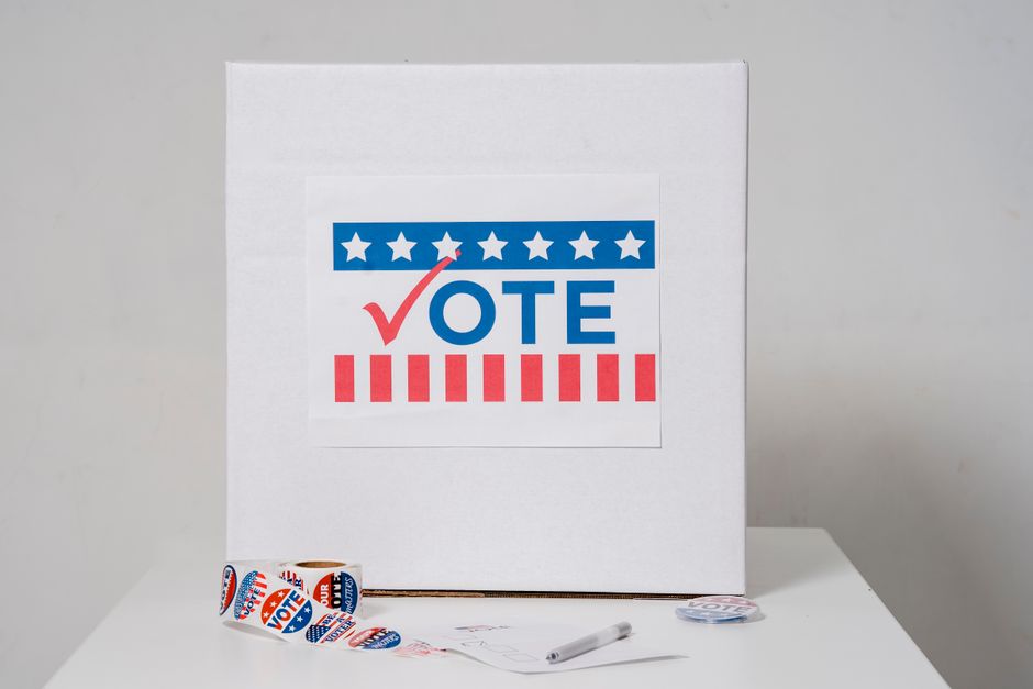 Ballot box with vote sign surrounded by voting stickers, indicating election theme.
