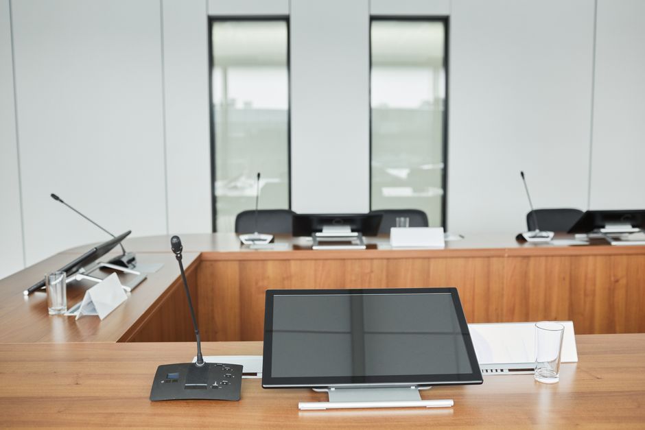 Empty conference room setup with microphones, monitors, and sleek wooden tables ready for meetings.