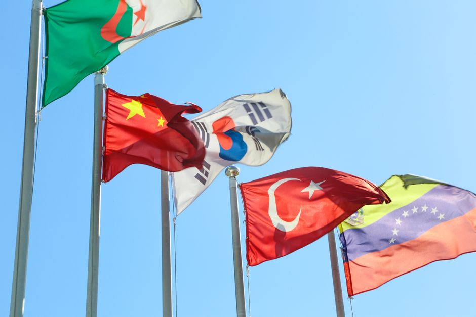 Five national flags from different countries waving on flagpoles under a clear blue sky