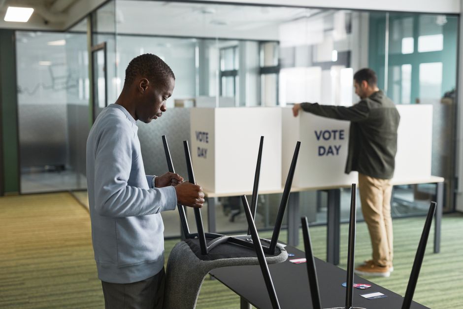 Men preparing voting booths indoors for election day, enhancing democracy.