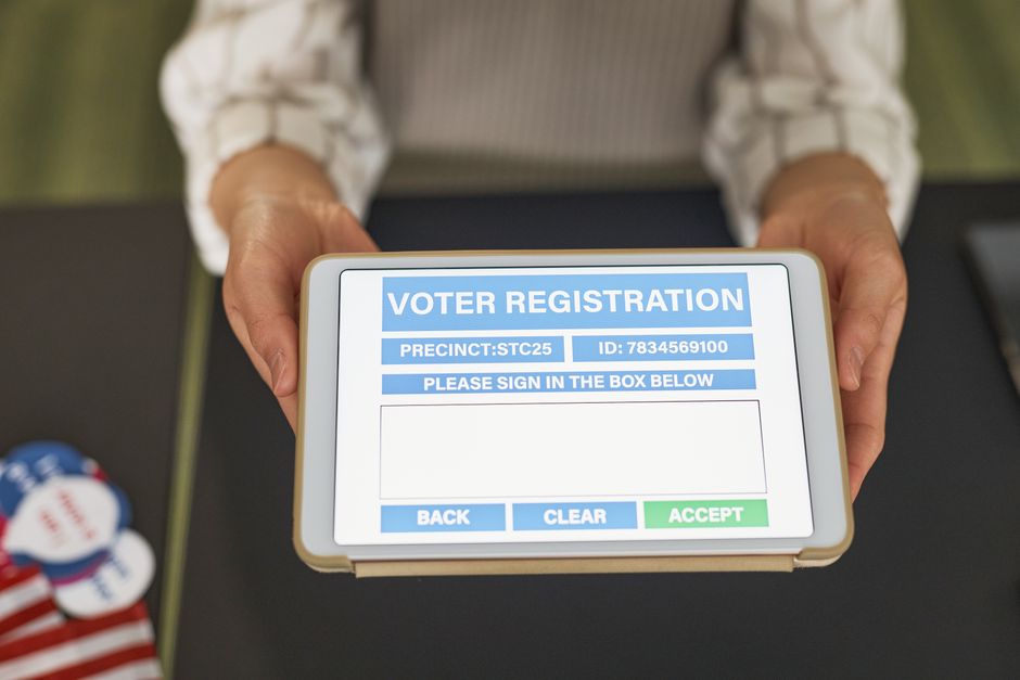 Close-up of hands holding a tablet displaying digital voter registration form.