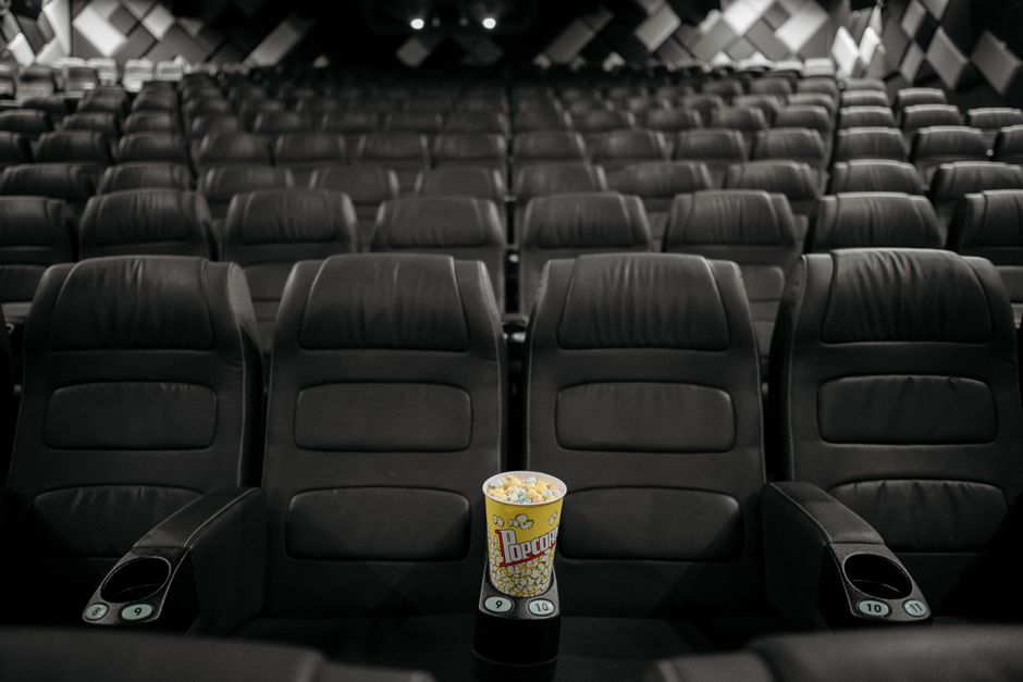 An empty cinema hall with black leather seats and a bucket of popcorn on an armrest.