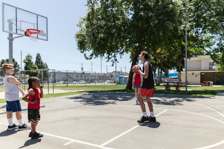 Kids playing basketball on an outdoor court on a sunny day, focusing on teamwork and fun.