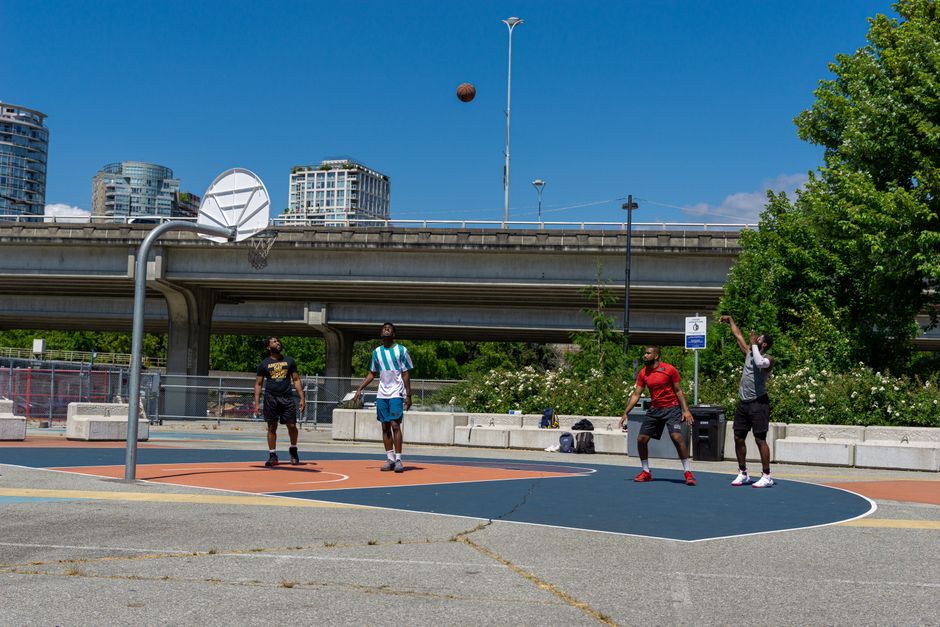 Group of friends playing basketball on an outdoor urban court beneath a city bridge.